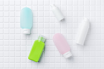 Travel size cosmetic bottles for cream, lotion, shampoo, tonic, serum, oil. White tile background.