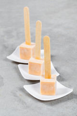 Apricot ice creams in the shape of small cubes on a wooden sticks. On a plate. Light gray background