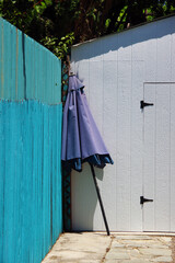 A closed purple parasol umbrella leaning against a turquoise fence