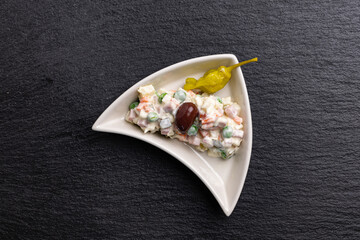 Fototapeta na wymiar A Bulgarian variation of Olivier salad known as Ruska Salata, a traditional dish in the Balkans, presented in a triangle-shaped bowl and adorned with an olive and marinated banana pepper.