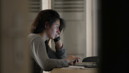 Woman browsing internet in front of laptop at home, candid authentic scene of person in front of computer screen late at night