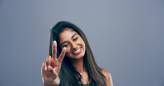 Indian, woman and happy with hands for peace, sign or freedom emoji in gray background, studio or mockup. V, symbol and funny portrait with a gesture and smile, icon or gen z profile picture