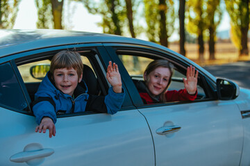 Happy mother and son waving hands from car window