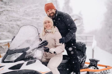 Fotobehang A couple, a man and a woman, on a snowmobile in a winter forest © Александр Лобач