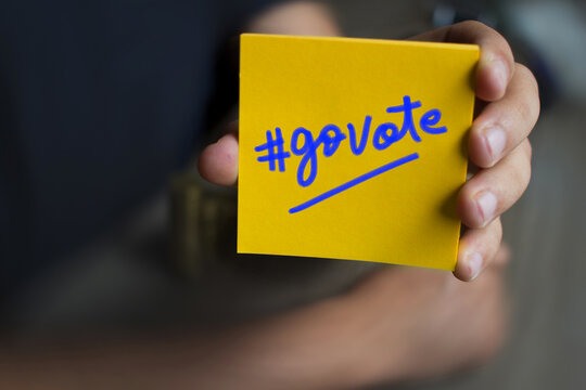 Hand holding an orange Paper with the word Go Vote 