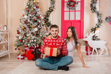 A beautiful couple on a Christmas background gives each other gifts. Young man and woman are preparing for the holiday.