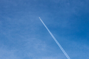 Blue sky and a plane with a white trail behind it. The plane and its trail are high in the sky.