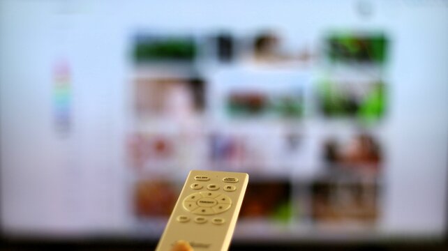 mando a distancia blanco con television  de fondo mostrando la programacion de la tele a la carta.