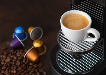 Cup with hot aroma coffee from espresso machine pods on dark background.