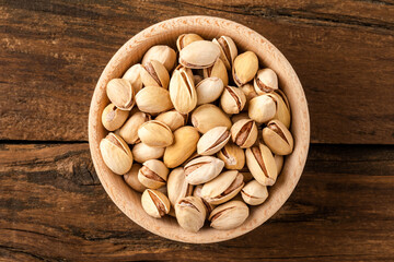 Overhead shot of roasted pistachios in bowl on wooden table. Healthy snacks