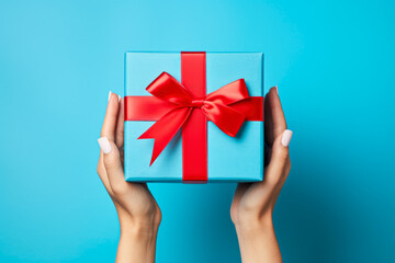 Female hands holding a blue gift box with a red bow on a blue background