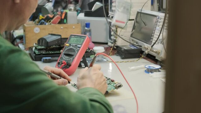 Electronic equipment repair shop. The Engineer Technician solders the printed circuit board of an electronic device under a microscope.