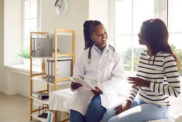 Happy smiling woman patient talking with friendly african american female doctor therapist holding...