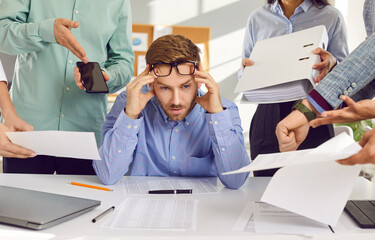 Very busy man suffering at work. Stressed, tired young business man sitting at his office desk,...
