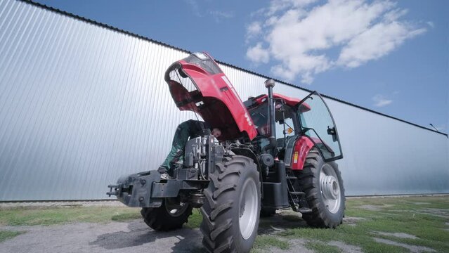 Farmer mechanic repairing tractor. Open tractor hood, engine. Repair agricultural technology