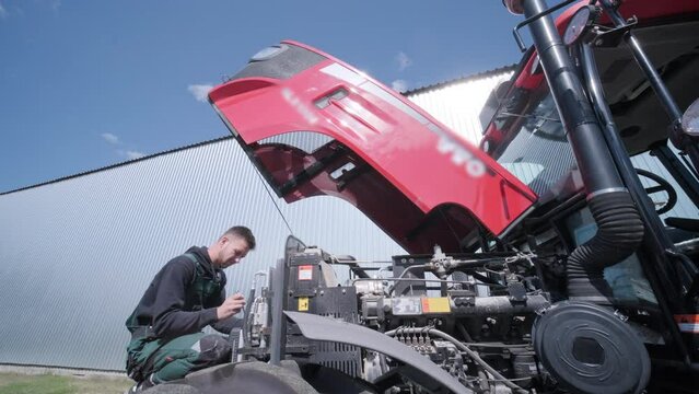 Farmer mechanic repairing tractor. Open tractor hood, engine. Repair agricultural technology