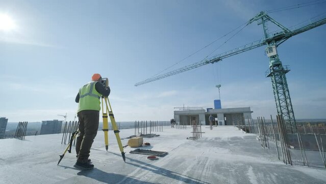 Geodetic works. Surveyor engineer in protective wear and red helmet using geodetic equipment at construction site. Professional equipment.