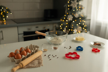 On the kitchen table there is a bowl with flour, a whisk, spices and molds for making Christmas cookies