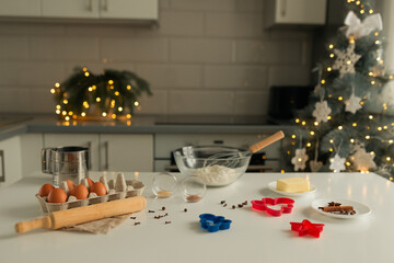 On the kitchen table there is a bowl with flour, a whisk, spices and molds for making Christmas cookies