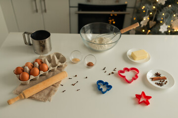 On the kitchen table there is a bowl with flour, a whisk, spices and molds for making Christmas cookies