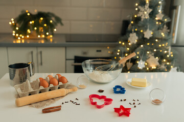 On the kitchen table there is a bowl with flour, a whisk, spices and molds for making Christmas cookies