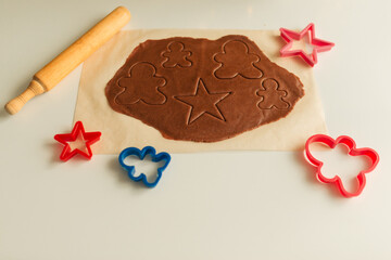 Rolled out dough lies on parchment paper with molds and rolling pin for cutting
