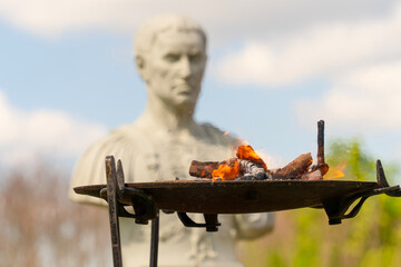 Ancient Roman sacrificial fire to the Roman gods with a Roman statue in the background.