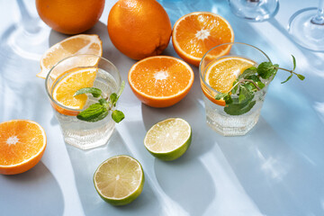 Summer orange cocktails with citrus fruits on blue background. Hard seltzer, lemonade, refreshing drinks, low alcohol mocktails, summer party concept. Trendy palm leaf shadow and sunlight, sun.