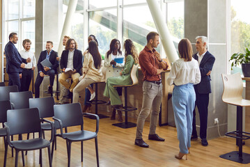 Full length photo of a group of diverse business people men and women chatting after meeting. Company employees or group of staff talking in modern office or conference room discussing work project. - obrazy, fototapety, plakaty