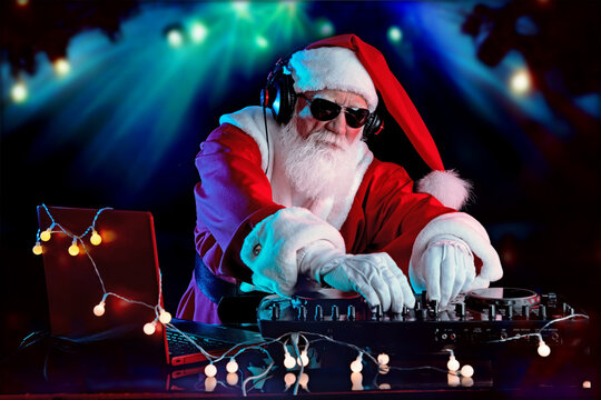 DJ Santa Claus mixing tracks in a nightclub at a Christmas and New Year party or Corporate events. Senior disc jockey as Santa listening music, headphones, laptop, mixer controller player, turntable