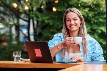 Seated in the cafe's garden, a young woman in her 30s combines her freelance work with a moment of...