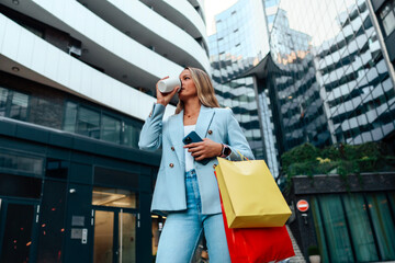 In the cityscape, a businesswoman carrying shopping bags effortlessly juggles her phone, coffee,...