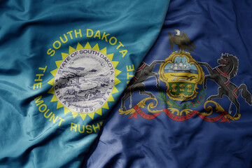 big waving colorful national flag of pennsylvania state and flag of south dakota state .