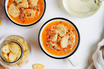 Roasted butternut squash soup with cream and pumpkin seeds on two white mugs.