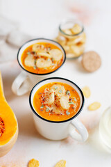 Roasted butternut squash soup with cream and pumpkin seeds on two white mugs.