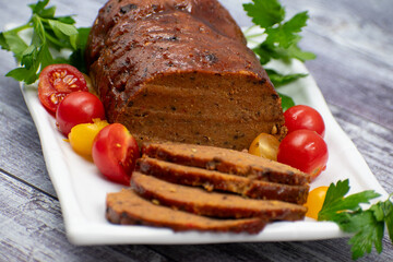Vegan meat alternative- seitan seasoned with spiced, glazed with BBQ sauce. White plate, sliced, wooden table.