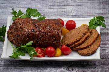 Vegan meat alternative- seitan seasoned with spiced, glazed with BBQ sauce. White plate, sliced, wooden table.