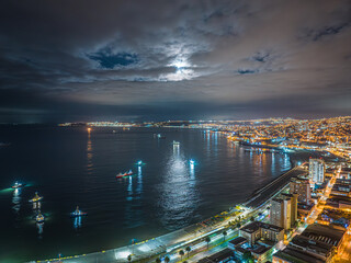 Vista aérea noturna da região do Terminal Pacífico Sur Valparaíso com lua cheia escondida entre nuvens e barcos ao redor.