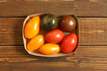 Yellow, green and red tomatoes in a cardboard box on a wooden table. View from above