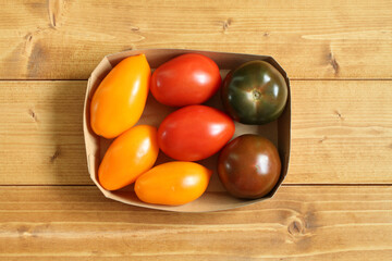 Yellow, green and red tomatoes in a cardboard box on a wooden table. View from above