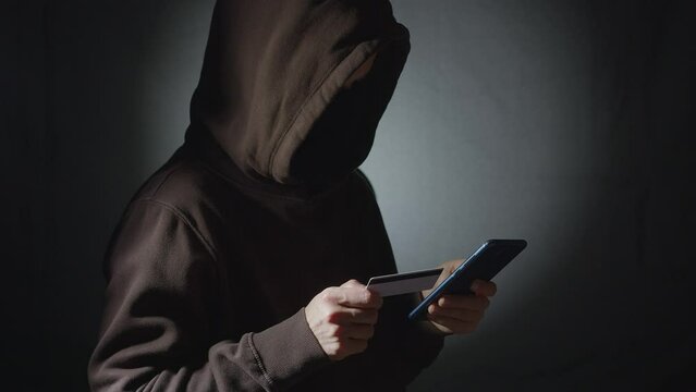 Male hacker using phone and credit card.