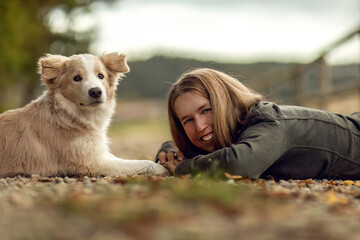 A young woman and her border collie puppy dog cuddling and interacting together in autumn outdoors, dog and owner concept - obrazy, fototapety, plakaty