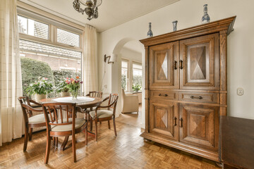 a dining room with wood flooring and wooden furniture in the center of the room is a large window...