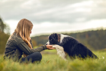 A young woman and her border collie puppy dog cuddling and interacting together in autumn outdoors,...