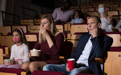 caucasian family in mask sitting at premiere in cinema