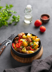 Fried pork meat with potatoes, onions and peppers. National homemade Georgian dish ojakhuri in a black frying pan on a dark background