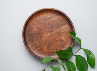 Modern empty product display. Minimal wooden round plate with green leaves on a gray background. Showcase concept with stage for product presentation, sale or cosmetics advertising banner.