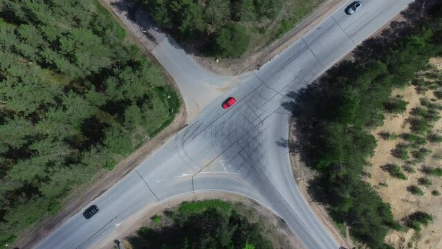 Road junction surrounded by trees, shrubs taken by drone. Cars drive along highway intersection in forest, countryside. Summer, sunny day. Aerial view of traffic on roadway crossing. 4K UHD 2160p
