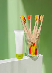 Wooden bamboo toothbrushs and tubes of toothpaste in a glass beaker on green background. Natural organic dental tooth care protection. Zero waste concept, banner. Teeth care. Mock up, template