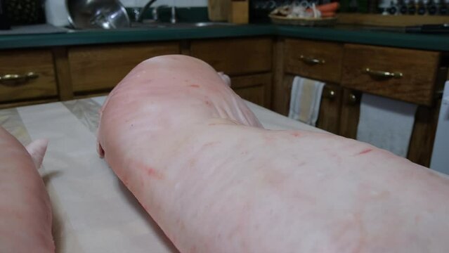 Close up of pork butt and mowing camera away exposing two halves of freshly butchered hog placed belly down on table ready for processing and portioning.